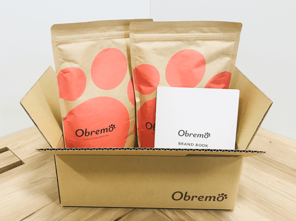 Obremoと書かれた段ボールの中に、Obremoのパッケージとブランドブックが入っている写真。