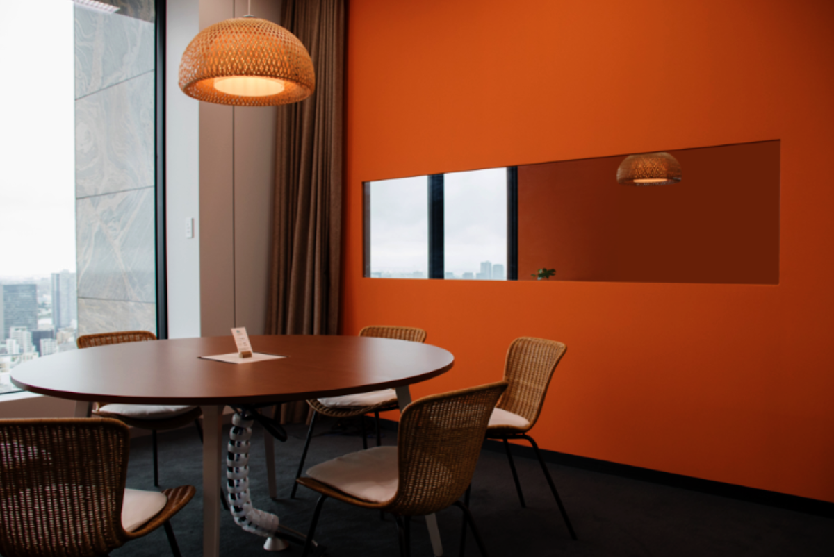 リサーチラボの室内の様子。オレンジ色の壁に大きな横型の鏡がはめこまれており、机には椅子が6脚置かれている。