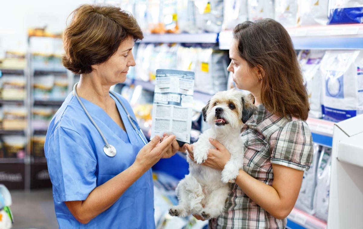 犬を抱いた女性と医師が、向き合って袋を見ている写真。