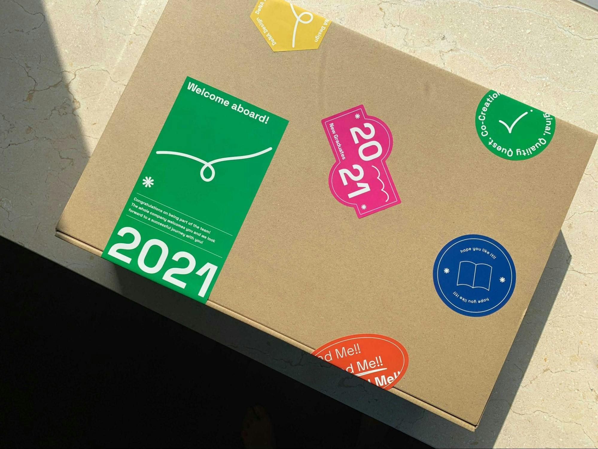 新卒メンバーの自宅に送付した箱の外装の写真。「2021」と書かれたものなどカラフルなシールが5枚貼られている。